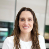 Charlotte Hunter is Registered Nutritional Therapist and adovates the use of Noops Nootropics for braincare. Charlotte has long, wavy brown hair, smiling warmly at the camera. She is wearing a white top and is positioned in an indoor setting with a blurred modern office or professional environment in the background